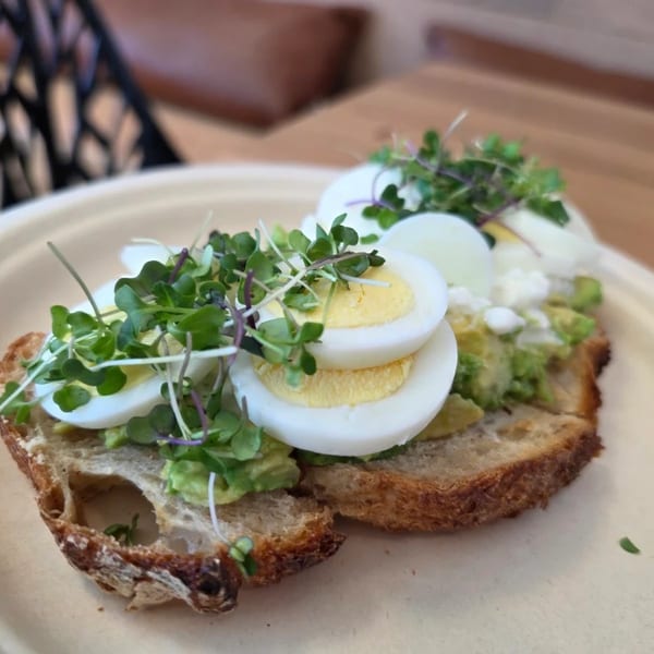 Avocado toast topped with sliced hard-boiled eggs, feta cheese, and microgreens on a white plate.