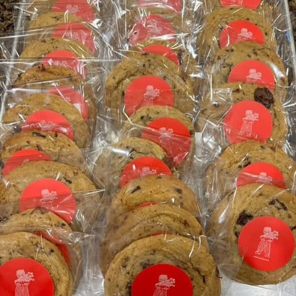 Rows of individually wrapped chocolate chip cookies with red circular stickers on a silver tray.