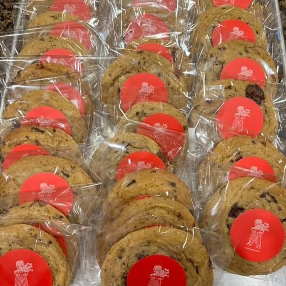 Rows of individually wrapped chocolate chip cookies with red circular stickers on a silver tray.