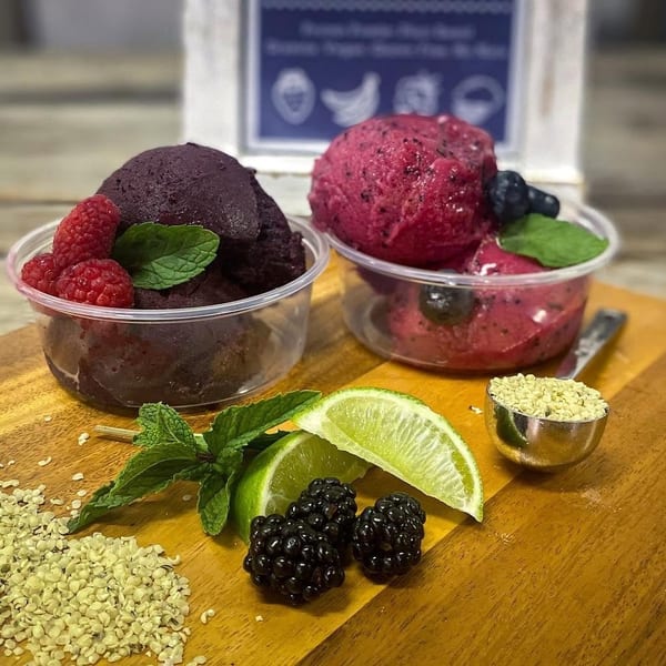 Two fruit sorbets in clear cups, garnished with berries and mint, alongside lime, blackberries, and hemp seeds.