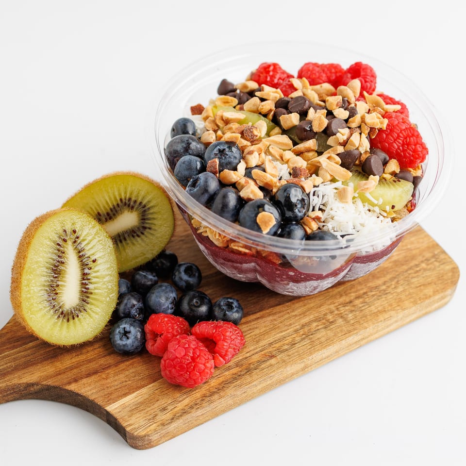A colorful acai bowl with blueberries, raspberries, kiwi, nuts, and chocolate chips on a wooden board.