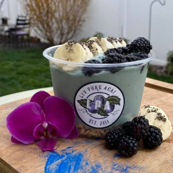 A Liv Pure Acai bowl with bananas, blackberries, and chia seeds, next to a purple orchid.