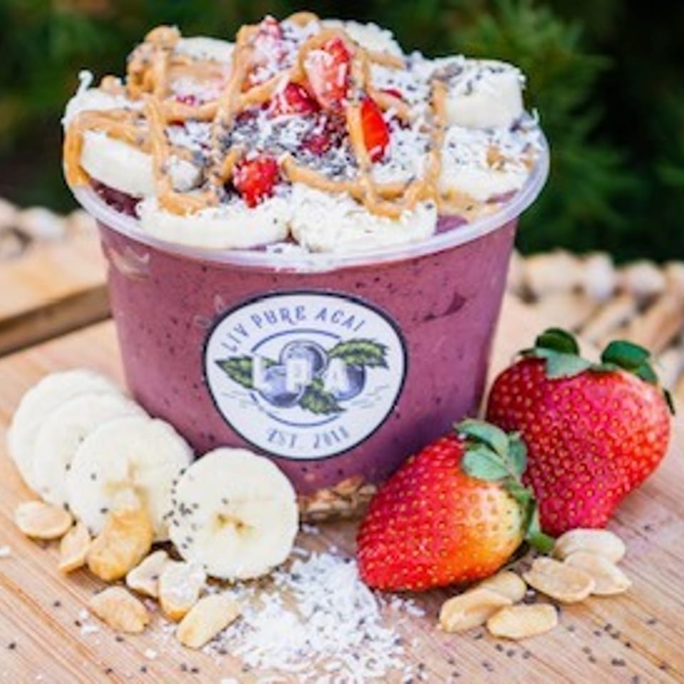 Acai bowl topped with bananas, strawberries, peanut butter, and chia seeds, next to fresh fruit.