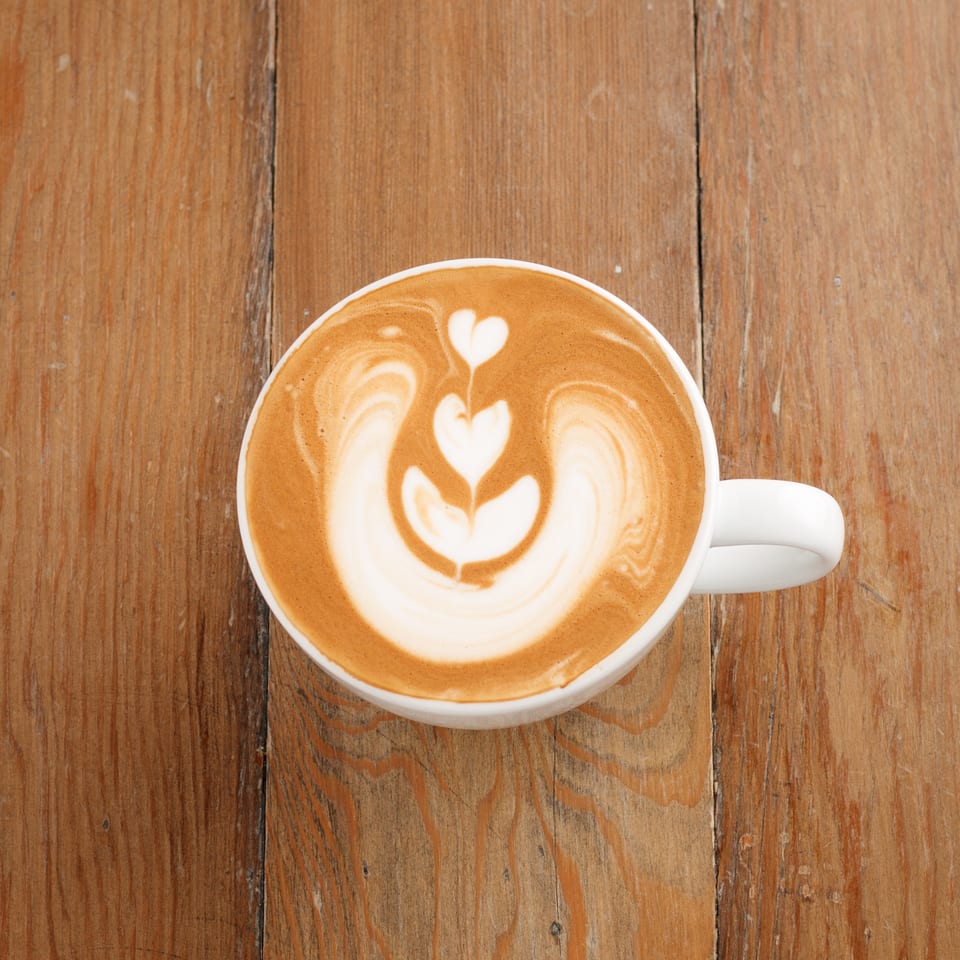 A white mug of latte with heart-shaped foam art sits on a rustic wooden table.