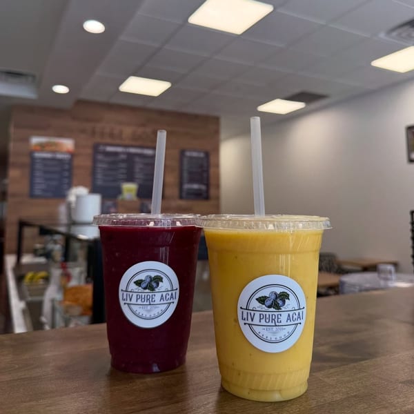 Two Liv Pure Acai smoothies, one purple and one yellow, on a wooden counter inside the restaurant.