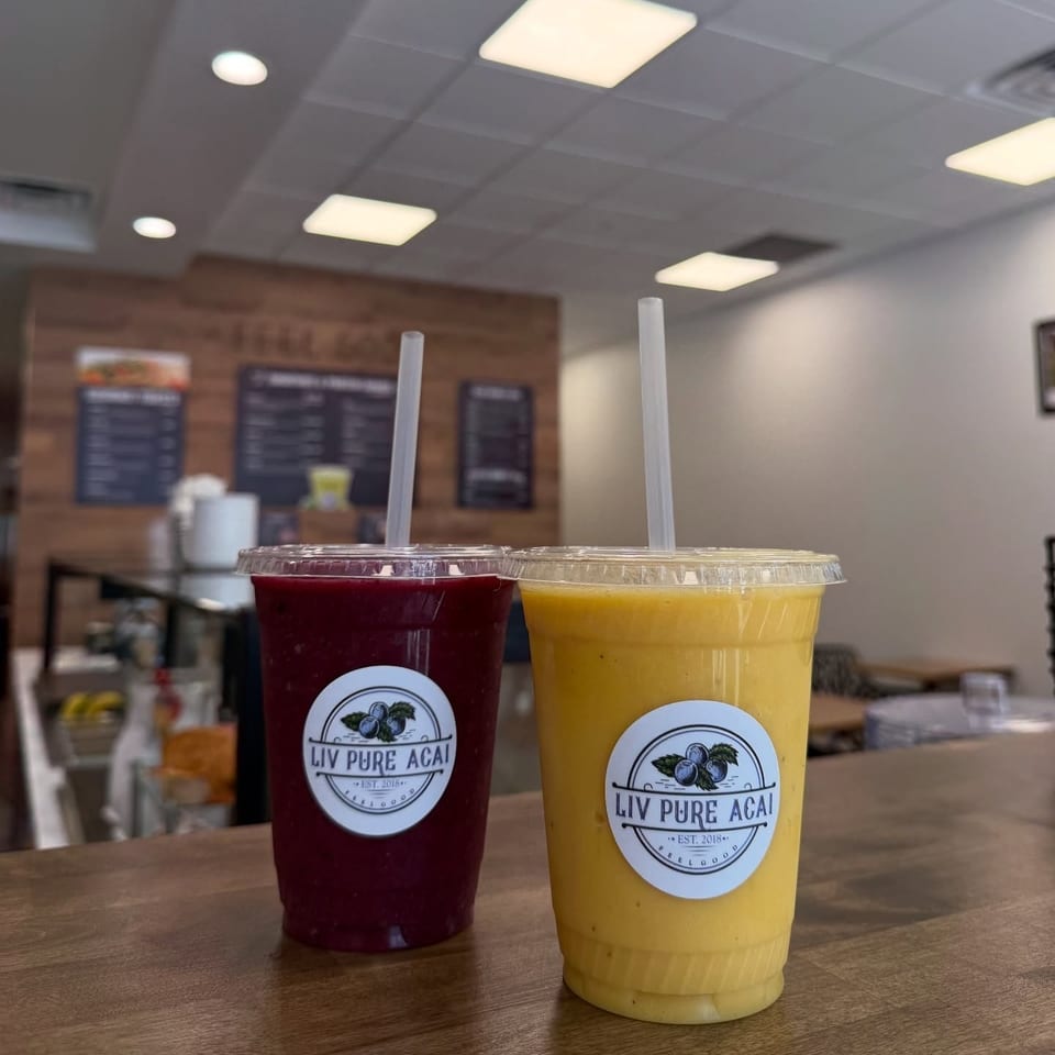 Two Liv Pure Acai smoothies, one purple and one yellow, on a wooden counter inside the restaurant.