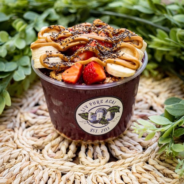 Liv Pure Acai bowl with bananas, strawberries, peanut butter, and chia seeds on a woven mat.