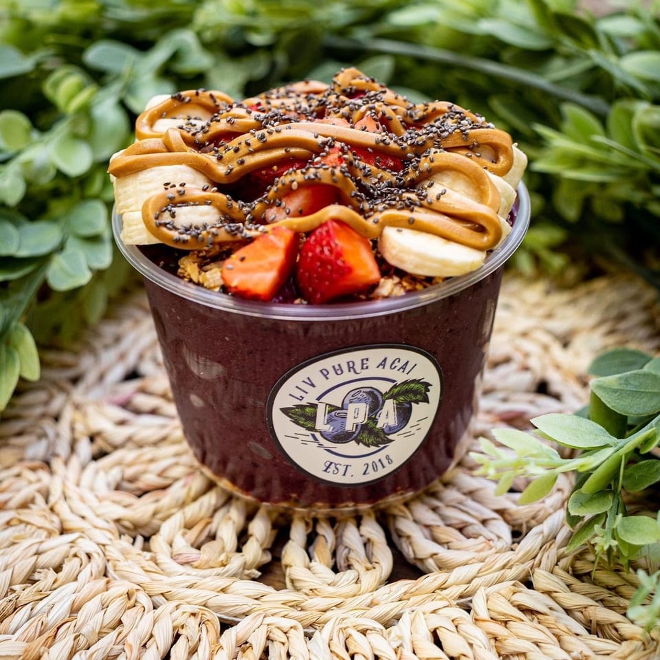 Liv Pure Acai bowl with bananas, strawberries, peanut butter, and chia seeds on a woven mat.