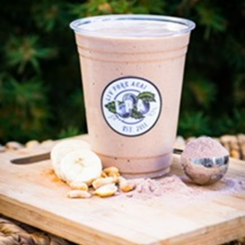 A Pure Açai smoothie with banana slices, peanuts, and powder on a wooden board.