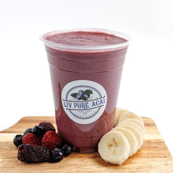 Liv Pure Acai smoothie with berries and sliced bananas on a wooden board.