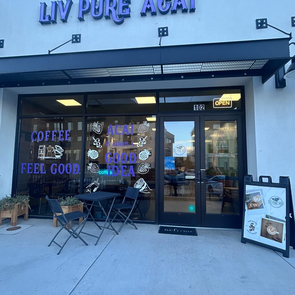 Liv Pure Acai storefront with blueberry logo, outdoor seating, coffee-themed window graphics, and an open sign.