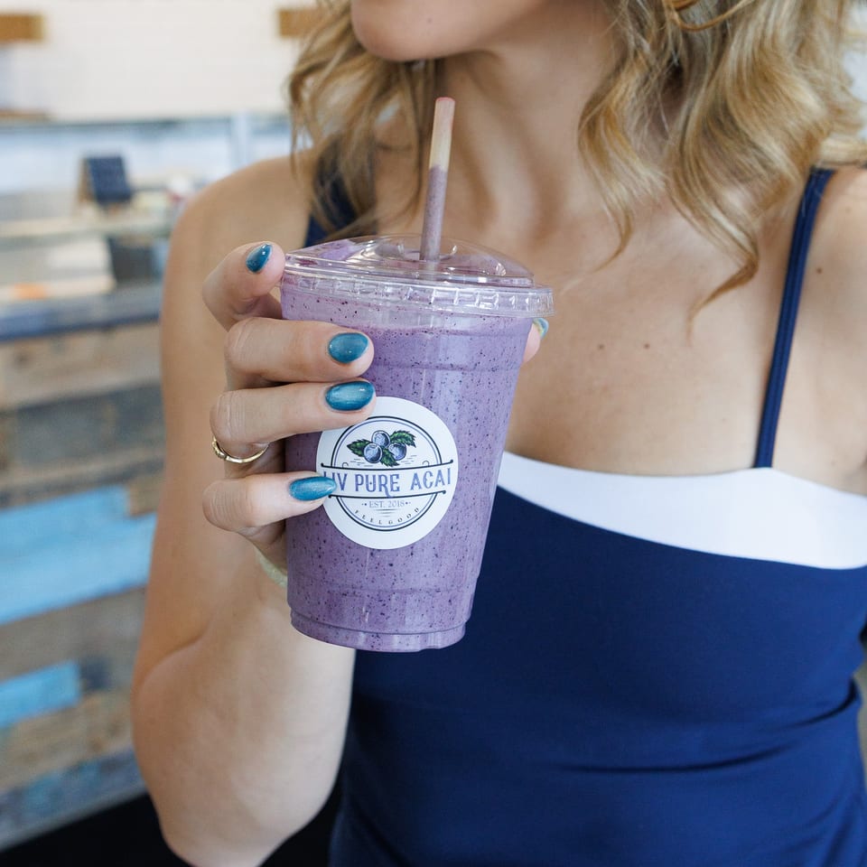 Woman with red lipstick and teal nails holding a purple smoothie with a "My Pure Acai" logo.