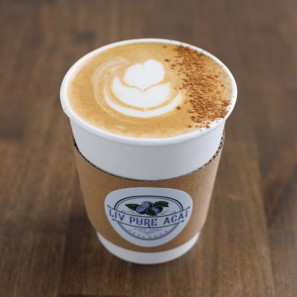 Foamy cappuccino with heart-shaped latte art and cinnamon dusting in a branded takeaway cup on a wooden table.