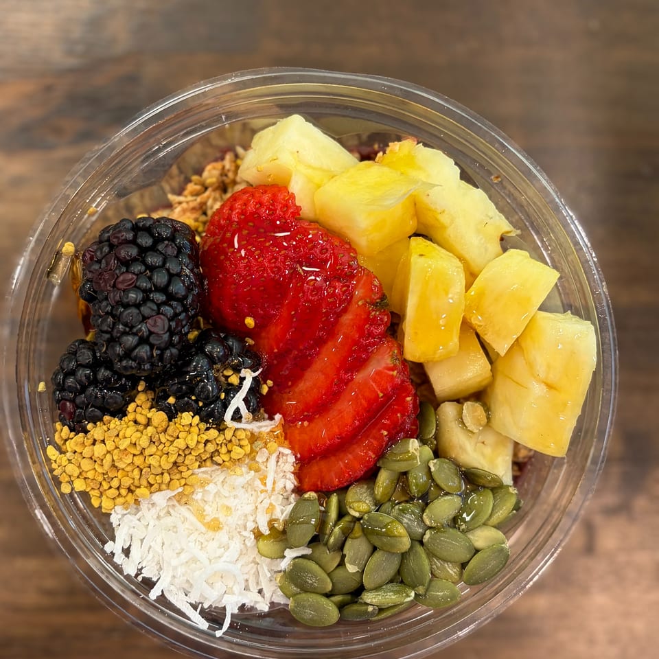A vibrant fruit bowl in a clear plastic cup, topped with blackberries, strawberries, pineapple, and seeds.