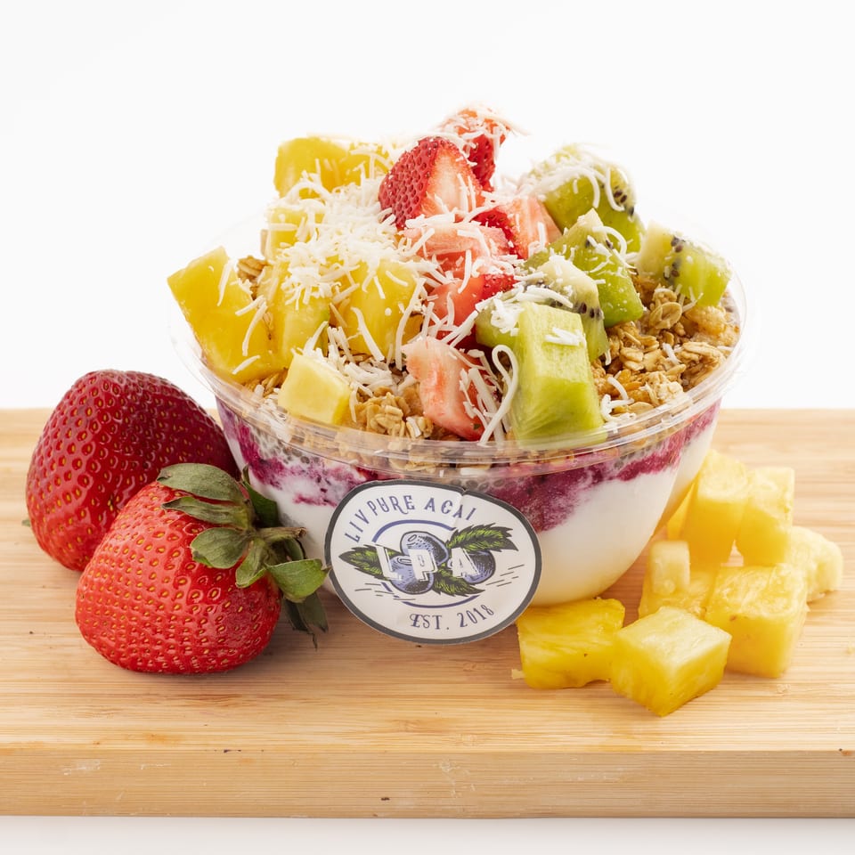 Liv Pure Acai bowl with strawberries, pineapple, kiwi, granola, and shredded coconut on a wooden board.