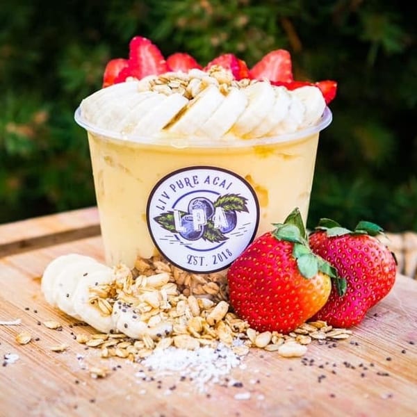 Liv Pure Acai smoothie bowl with bananas, strawberries, granola, and chia seeds on a wooden board.