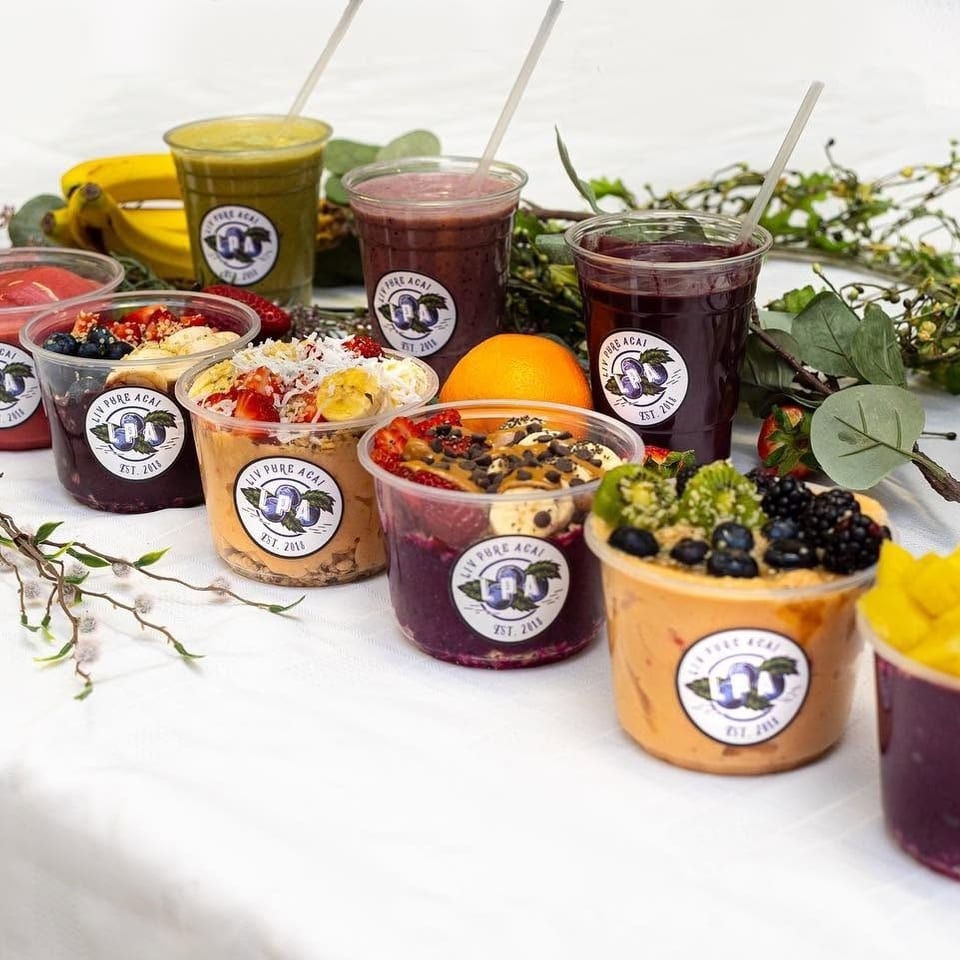 A variety of Liv Pure Acai bowls and smoothies with fruit toppings on a white tablecloth.