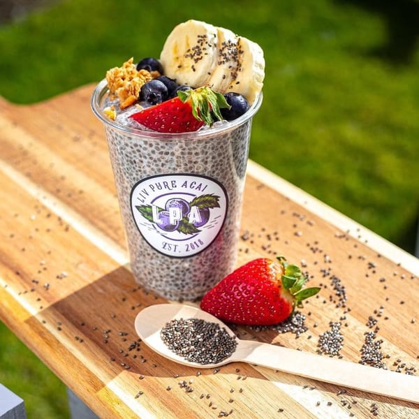 Liv Pure Acai chia pudding cup with fruit, granola, and a strawberry on a wooden board.