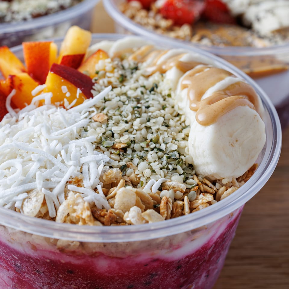 Close-up of a vibrant berry smoothie bowl topped with peaches, coconut, granola, bananas, and peanut butter.